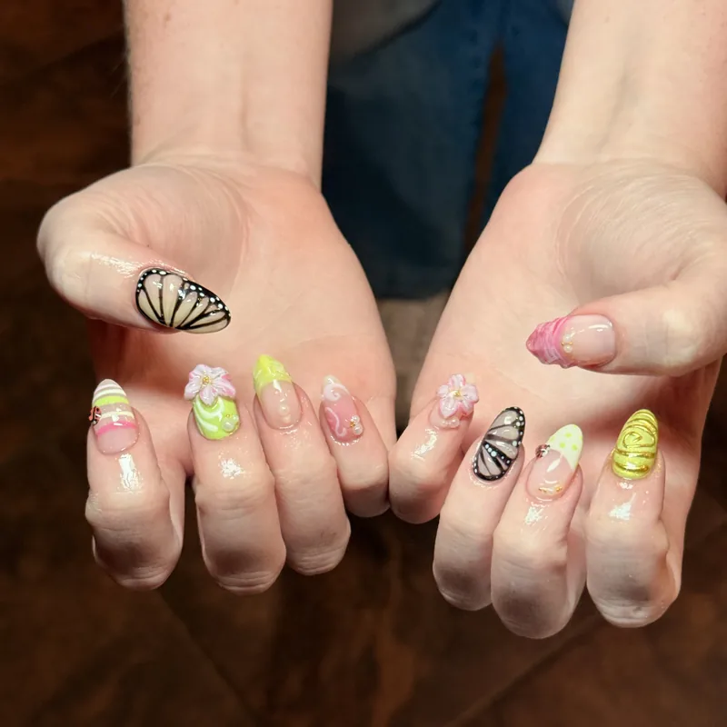 Hand-painted butterfly nail art in pastel green, pink and yellow on almond-shaped nails.