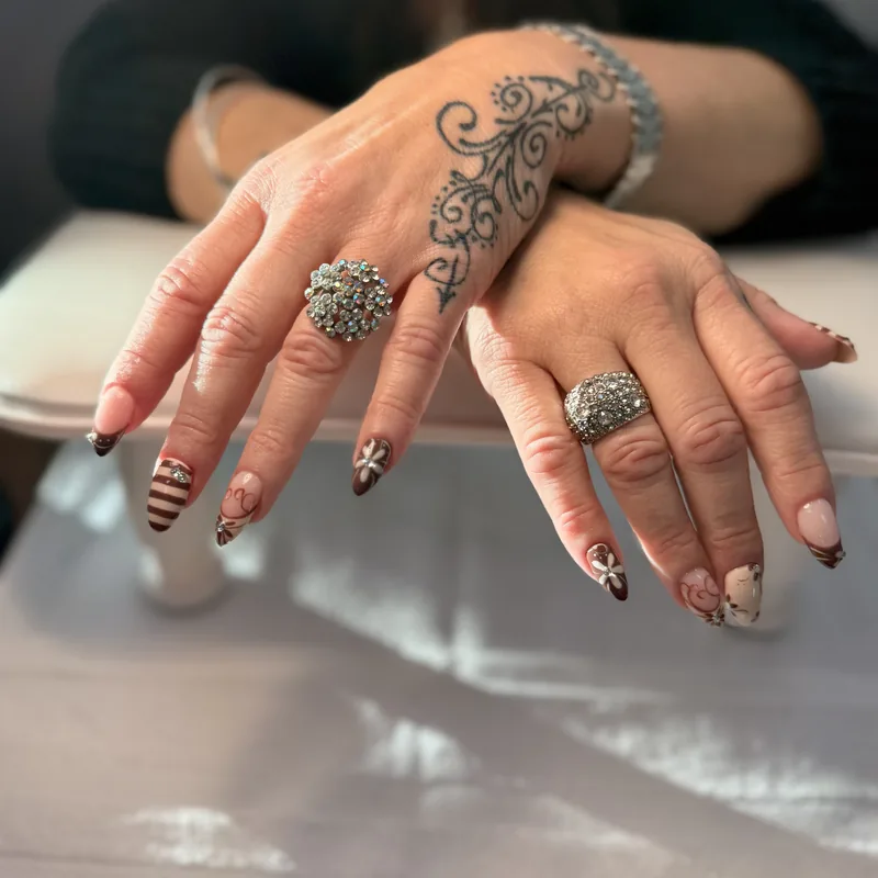 Almond nails in cocoa brown with hand-painted florals, stripes and rhinestone accents.