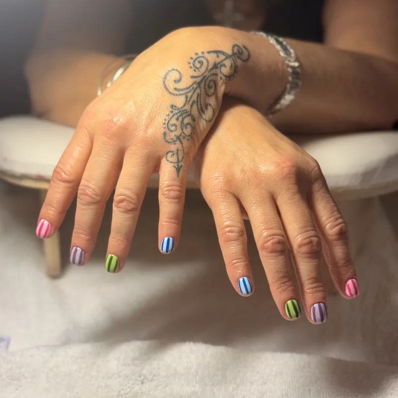 Short almond nails painted with multicoloured pastel stripes in blue, green, pink and yellow.