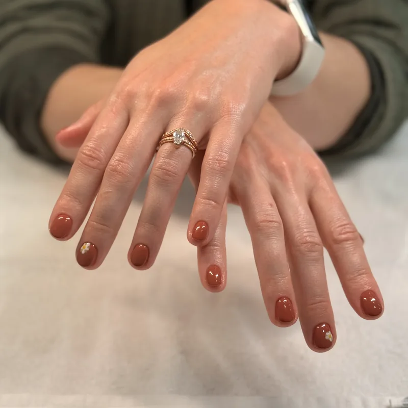 Short almond nails in a glossy terracotta brown.